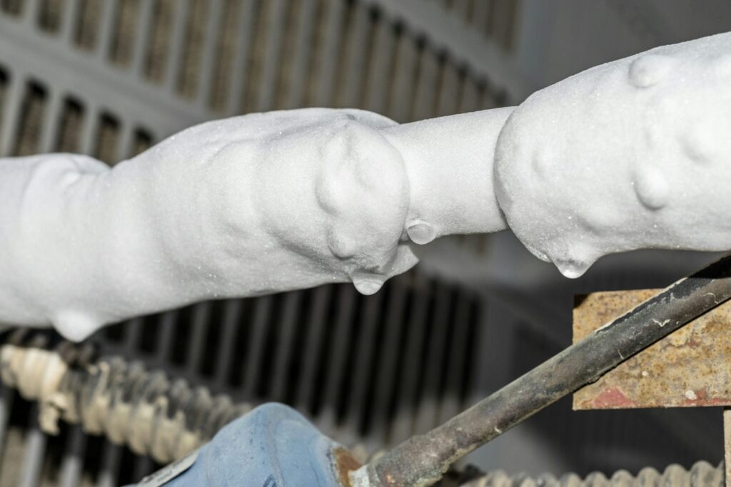 Close-up of an air conditioner's copper refrigerant lines completely frozen over with thick white ice buildup, a clear sign of an AC unit freezing up.