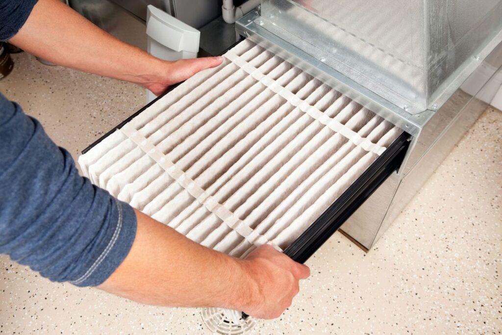 Homeowner safely changing a clogged furnace filter to reduce AC system strain