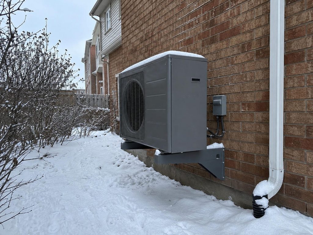 Outdoor heat pump unit mounted beside a suburban Ontario home with snow on the ground.