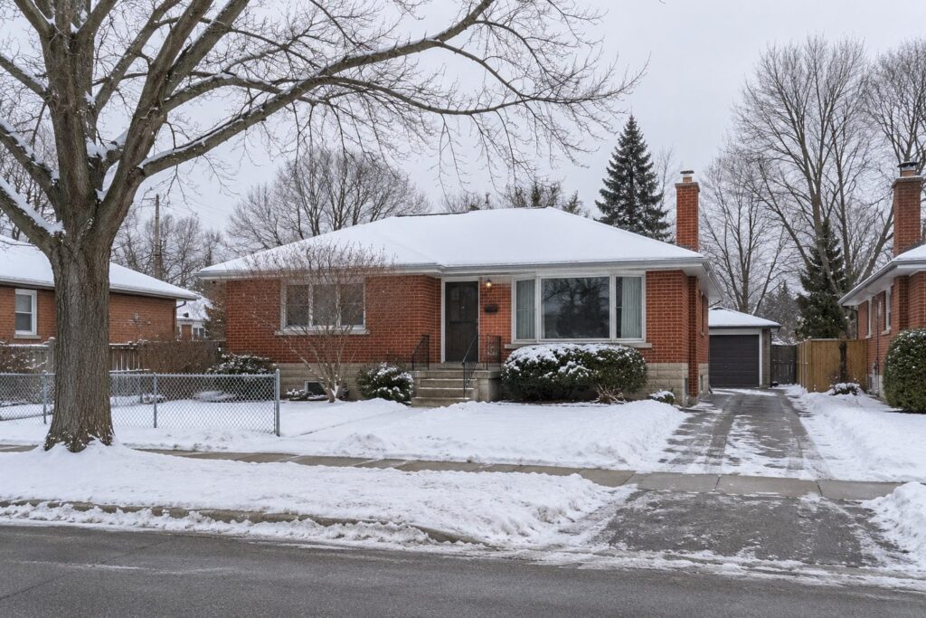 Post war red brick bungalow with a snow covered lawn and driveway on a quiet Greater Toronto Area street in winter